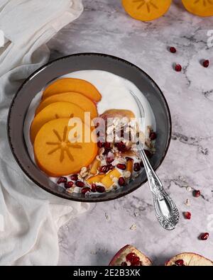 Nourriture saine, petit déjeuner, persimmon frais avec grenade et flocons d'avoine joliment disposés sur une table en marbre Banque D'Images