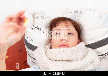 une jeune fille enveloppée d'un foulard est malade à la maison, se trouve dans le lit et tient une capsule avec des médicaments dans sa main Banque D'Images