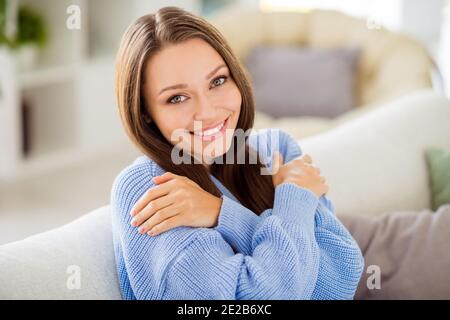 Portrait d'une jolie fille gaie assise sur un divan s'embrassant des vêtements confortables dans un appartement lumineux à l'intérieur Banque D'Images