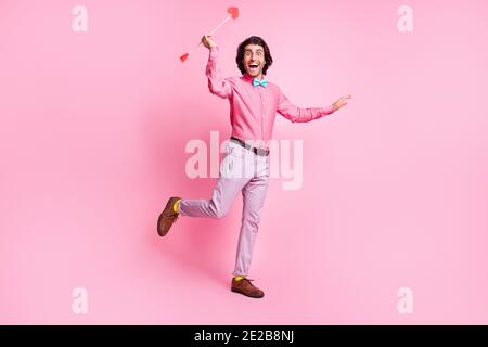 Photo pleine longueur de l'homme de cheveux brunet gai et tordus mains bras flèches cupid isolé couleur rose fond Banque D'Images