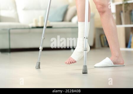 Vue latérale d'une femme handicapée avec pied bandé marche avec béquilles à la maison Banque D'Images