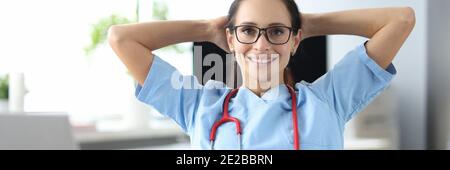 Jeune médecin souriant assis à table par ordinateur portable et tenant rendez-vous en clinique Banque D'Images