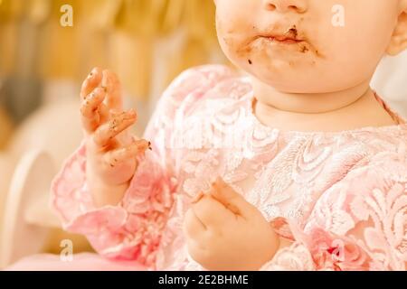 une petite fille s'assoit à la table et mange seule. enfant aux mains et à la bouche sales Banque D'Images