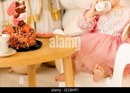 une petite fille s'assoit à la table et mange seule. enfant tenant une soucoupe avec une tasse Banque D'Images