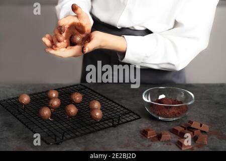 Jeune femme qui fabrique des truffes au chocolat. Arrière-plan sombre. Concept de cuisine délicieuse. Un design parfait pour toutes les applications. Banque D'Images