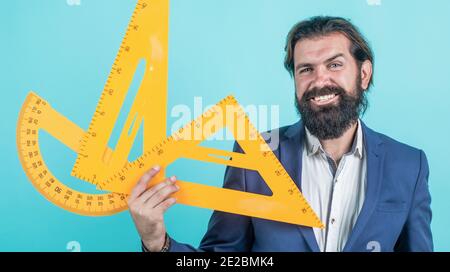 homme barbu mature enseignant en costume assis dans la classe d'école avec tableau noir, mesure. Banque D'Images