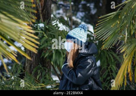 Photo d'une jeune femme dans un visage avec mise au point peu profonde masque et chapeau tricoté entouré de palmiers Banque D'Images
