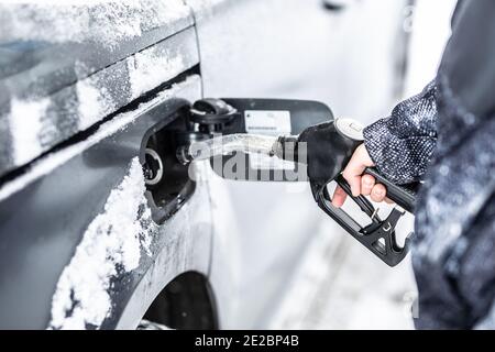 Main d'un homme qui remplit le réservoir de carburant de sa voiture pendant l'hiver gelé et enneigé. Banque D'Images
