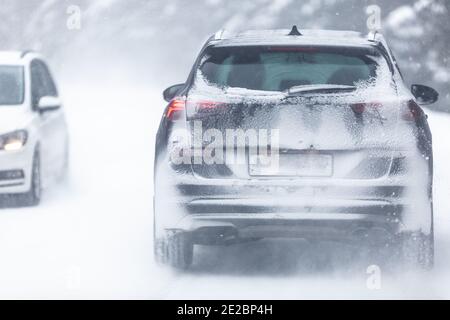 Véhicule utilitaire sport roulant sur une route enneigée et glissante à l'intérieur de la forêt, dont le numéro d'immatriculation est insivisible en raison de la neige. Banque D'Images