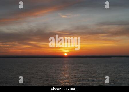 Beau coucher de soleil nuageux sur la mer juste comme le soleil touche l'horizon. Banque D'Images