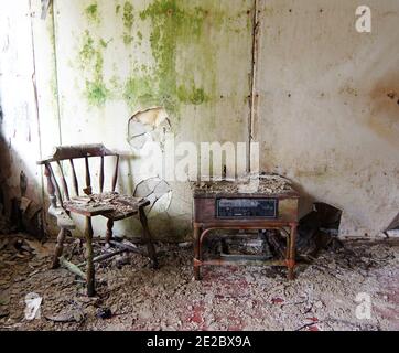 Endroit abandonné - chaise cassée et ancienne armoire radio dedans face d'un mur moussy Banque D'Images