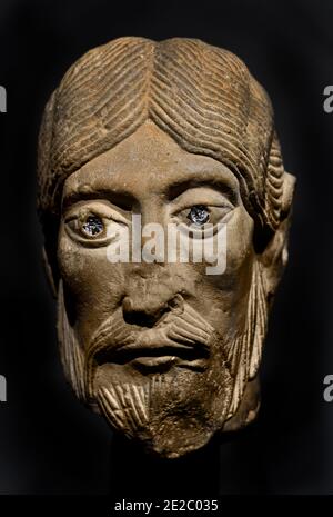 Une sculpture en calcaire du XIIe siècle représentant la tête d'un apôtre avec des yeux distinctifs incrustés de verre, originaire de la région de Bourgogne de France à la fin de la période romane, FRANCE, BOURGOGNE (période romane tardive, lorsque les figures devenaient plus naturalistiquement sculptées, cette tête d'apôtre est remarquable pour sa modélisation sensible des pommettes et des lèvres. Alors que les cheveux sont sculptés de la manière habituelle des incisions parallèles, le tressage est rendu avec une certaine élégance.) Banque D'Images
