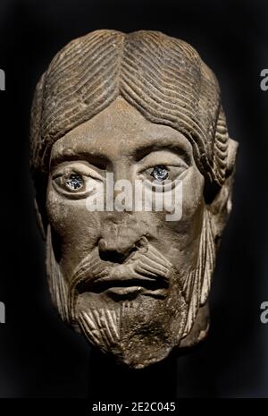 Une sculpture en calcaire du XIIe siècle représentant la tête d'un apôtre avec des yeux distinctifs incrustés de verre, originaire de la région de Bourgogne de France à la fin de la période romane, FRANCE, BOURGOGNE (période romane tardive, lorsque les figures devenaient plus naturalistiquement sculptées, cette tête d'apôtre est remarquable pour sa modélisation sensible des pommettes et des lèvres. Alors que les cheveux sont sculptés de la manière habituelle des incisions parallèles, le tressage est rendu avec une certaine élégance.) Banque D'Images