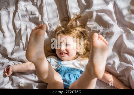 Gaie bébé riant.UNE fille gaie se trouve sur le lit et hurle avec joie/exercice et la forme physique couché sur le couvre-lit. Banque D'Images