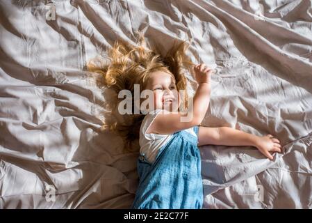 Gaie bébé riant.UNE fille gaie se trouve sur le lit et hurle avec joie/exercice et la forme physique couché sur le couvre-lit. Banque D'Images