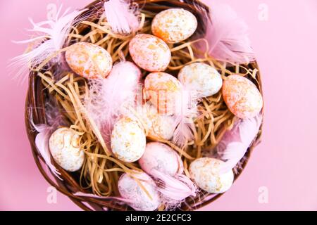 Composition de Pâques, décor traditionnel. Petit deon rose fond clair. Œufs colorés et plumes douces dans un panier en osier Banque D'Images