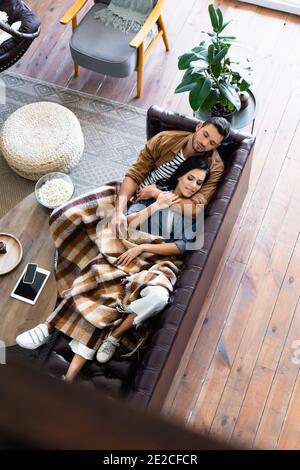 vue de dessus d'un jeune couple dormant sous une couverture à carreaux confortable sur canapé en cuir dans la salle de séjour Banque D'Images