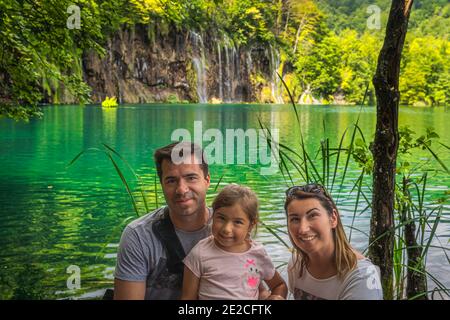 Portrait de famille heureuse avec lac et cascades en arrière-plan, en vacances dans le magnifique parc national des lacs de Plitvice, un site classé au patrimoine mondial de l'UNESCO Banque D'Images