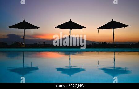 Vue sur la piscine au coucher du soleil avec silhouettes de parasol, vue depuis la terrasse du jardin sur le toit du Rosewood Hotel à Puebla de Zaragoza, au Mexique. Banque D'Images