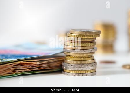 Pièces en euros empilées dans la pile et le tas de billets de banque couché sur une table blanche Banque D'Images