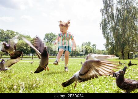 Petite fille scares pigeons jeu amusant été. Écologie, court sur l'herbe dans le parc de la ville à l'extérieur, style de vie