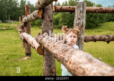 Enfants, filles se tenant à côté d'une clôture dans le village. Promenades à la campagne. Agriculture. Écologie et enfance heureuse, belle petite fille. Banque D'Images