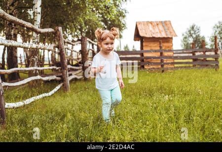 Enfants, filles se tenant à côté d'une clôture dans le village. Promenades à la campagne. Agriculture. Écologie et enfance heureuse, belle petite fille. Banque D'Images