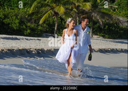 Un couple récemment marié célèbre son mariage sur une plage de l'île de Mustique aux Caraïbes. Main dans la main, ils éclaboussent dans le surf et détritus de la robe. Banque D'Images