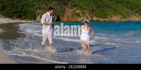 Un couple récemment marié célèbre son mariage sur une plage de l'île de Mustique aux Caraïbes. Main dans la main, ils éclaboussent dans le surf et détritus de la robe. Banque D'Images