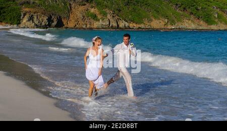 Un couple récemment marié célèbre son mariage sur une plage de l'île de Mustique aux Caraïbes. Main dans la main, ils éclaboussent dans le surf et détritus de la robe. Banque D'Images