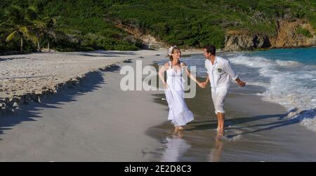 Un couple récemment marié célèbre son mariage sur une plage de l'île de Mustique aux Caraïbes. Main dans la main, ils éclaboussent dans le surf et détritus de la robe. Banque D'Images