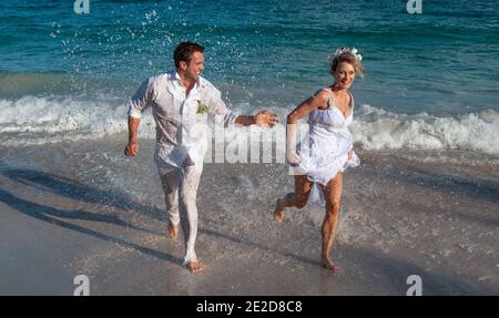 Un couple récemment marié célèbre son mariage sur une plage de l'île de Mustique aux Caraïbes. Main dans la main, ils éclaboussent dans le surf et détritus de la robe. Banque D'Images