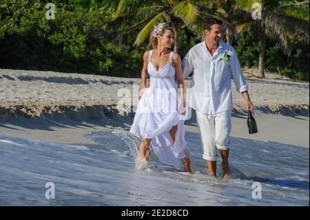 Un couple récemment marié célèbre son mariage sur une plage de l'île de Mustique aux Caraïbes. Main dans la main, ils éclaboussent dans le surf et détritus de la robe. Banque D'Images