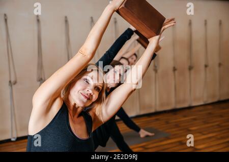 Groupe de femmes pratiquant l'étirement du yoga à l'aide de blocs de bois, exercice pour la flexibilité de la colonne vertébrale et des épaules Banque D'Images