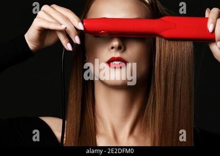 Jeune jolie femme avec de longs cheveux lisses soyeux en noir vêtements couvrant les yeux avec un lisseur rouge Banque D'Images