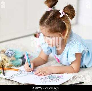 Calme concentré jeune fille est couché sur le dessin de tapis doux colorier des photos de poupées avec des crayons colorés Banque D'Images