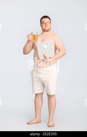 Homme en surpoids avec des écailles et un verre de bière sur fond gris. Concept de perte de poids Banque D'Images