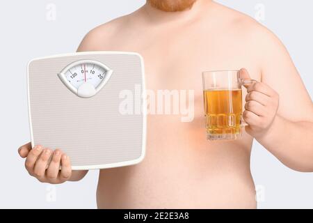 Homme en surpoids avec des écailles et un verre de bière sur fond gris. Concept de perte de poids Banque D'Images