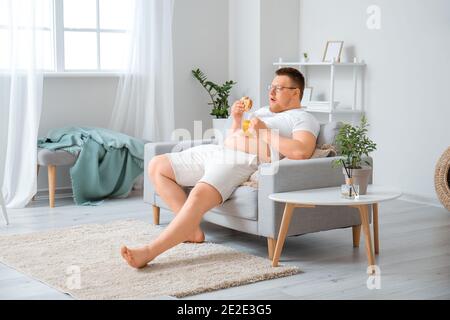 Homme en surpoids avec un hamburger malsain et un verre de bière à la maison. Concept de perte de poids Banque D'Images