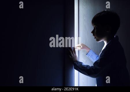 Un petit garçon piquant à travers la porte ouverte dans l'obscurité Banque D'Images