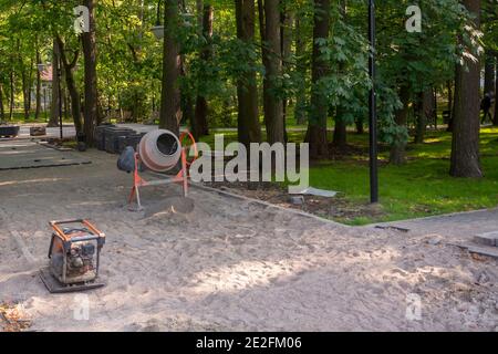 Réparation du trottoir dans le parc de la ville. Mélangeur de béton et plaque vibrante pour poser des dalles sur le sable. Mise au point sélective. Banque D'Images