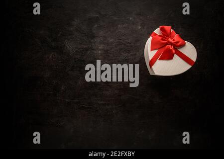 Boîte cadeau avec ruban rouge en forme de coeur et espace vide pour le texte sur fond noir Banque D'Images