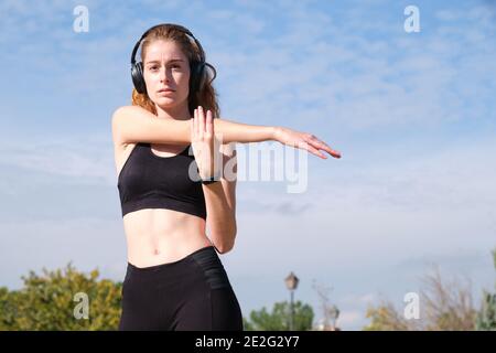 REDHEAD femme caucasienne avec des écouteurs qui étirent son bras. Fitness et sport en plein air. Banque D'Images