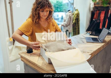 Femme préparant un paquet pour la livraison à la caisse du magasin de vêtements. femme d'affaires emballant des vêtements pour la livraison au magasin. Banque D'Images