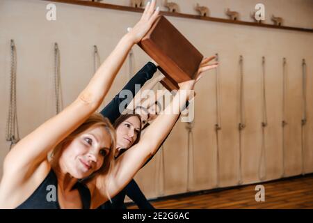 Groupe de femmes pratiquant l'étirement du yoga à l'aide de blocs de bois, exercice pour la flexibilité de la colonne vertébrale et des épaules Banque D'Images