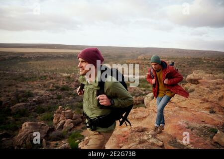 Jeunes randonneurs mâles avec sac à dos et montagne d'escalade de casquette d'hiver piste Banque D'Images