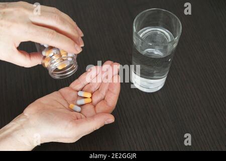 Femme avec des pilules dans les mains. Médicament en capsules et verre d'eau sur une table Banque D'Images