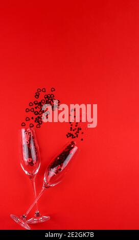 Deux verres de champagne remplis de paillettes en forme de coeur sur un fond rouge Saint-Valentin. Banque D'Images