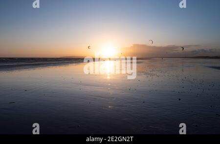 Cerfs-volants et surfeurs sur la côte sud à Camber Sands, East Sussex au coucher du soleil. Banque D'Images