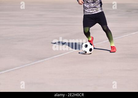 jambes d'un sportif méconnaissable jouant avec le ballon dans un terrain de football en béton, concept de style de vie sain et de sport urbain dans la ville, copie Banque D'Images